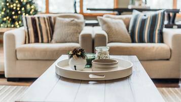 Un salon chaleureux avec un canapé beige, une table basse agrémentée d’objets décoratifs et un sapin de Noël en arrière-plan.