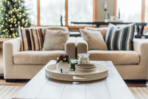 Una sala de estar acogedora con un sofá beige, una mesa de centro con objetos decorativos y un árbol de Navidad al fondo.