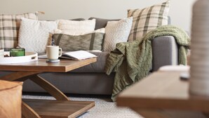 A cozy living room with a grey sofa, multiple cushions, a wooden coffee table, and a green knitted blanket.