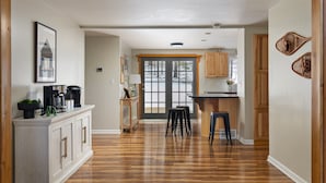 A spacious kitchen with wooden cabinets, a dining area with stools, and a large window with a view of trees.