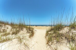 Een zandpad langs het strand met duinen en een helderblauwe lucht.