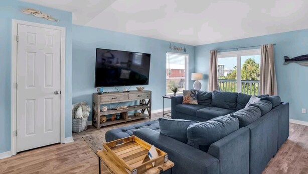 A living room with a sectional sofa, a flat-screen TV, a wooden coffee table, and a window with curtains. - Seashell Suite! (Destin)
