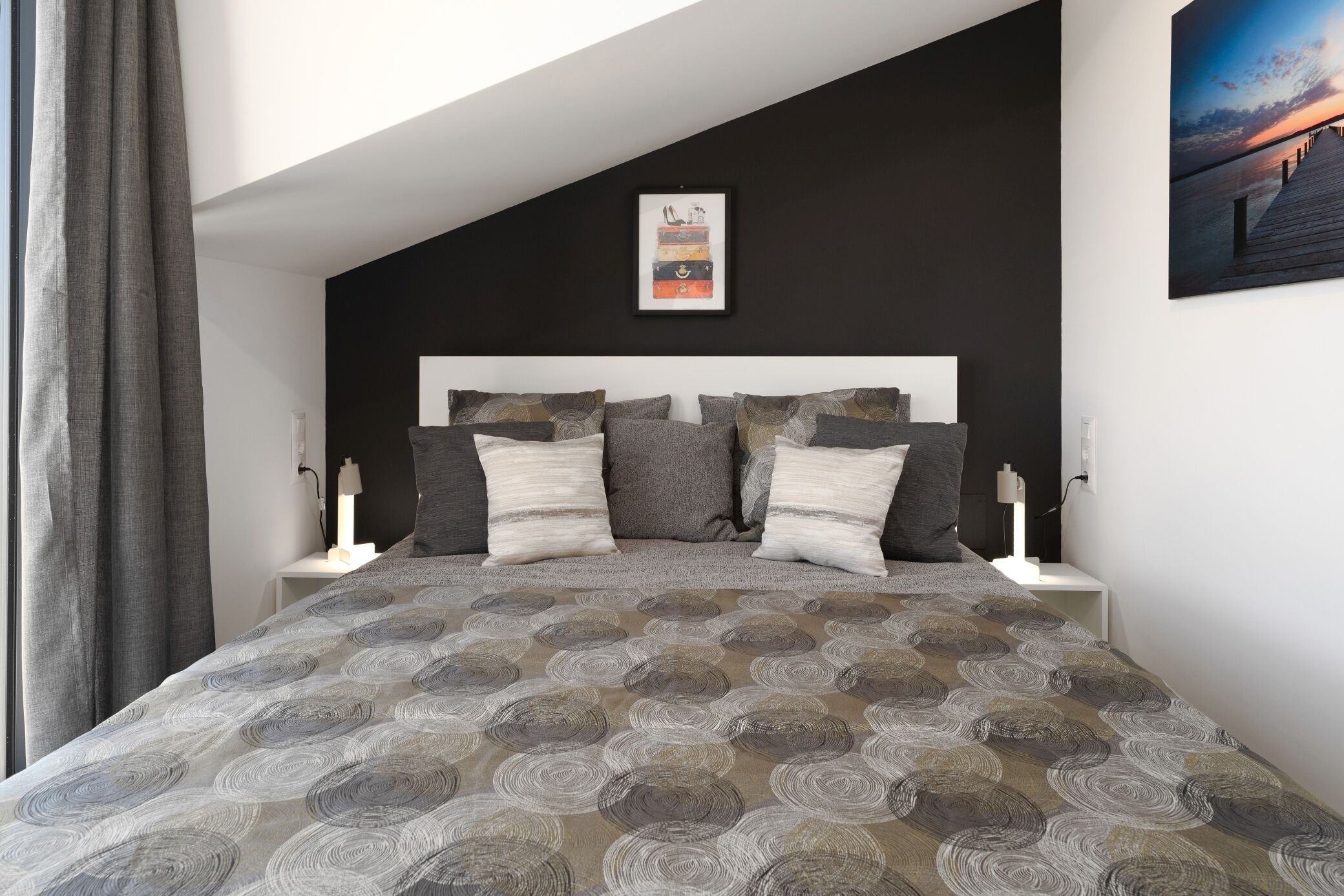 A bedroom with a bed, a headboard, a nightstand, a lamp, and a wall art piece.