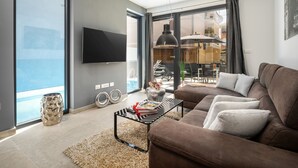 Een moderne woonkamer met een bruine bank, een glazen salontafel en een flatscreen televisie die aan de muur is bevestigd.