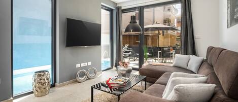 A modern living room with a brown sofa, a glass coffee table, and a flat-screen TV mounted on the wall.