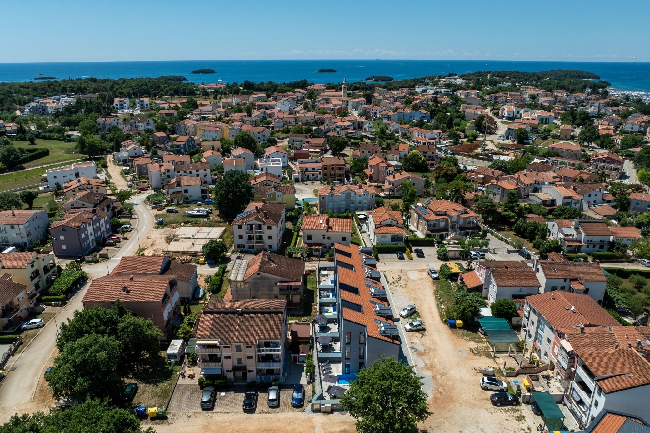 An aerial view of a coastal residential area with multiple buildings, roads, and a clear view of the sea.