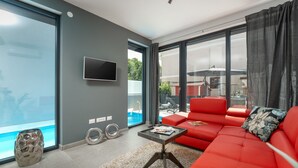 A modern living room with a red sofa, a glass coffee table, and a flat-screen TV mounted on the wall.