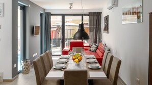 A dining area with a table set for six, a fruit bowl, and a red sofa in the background.