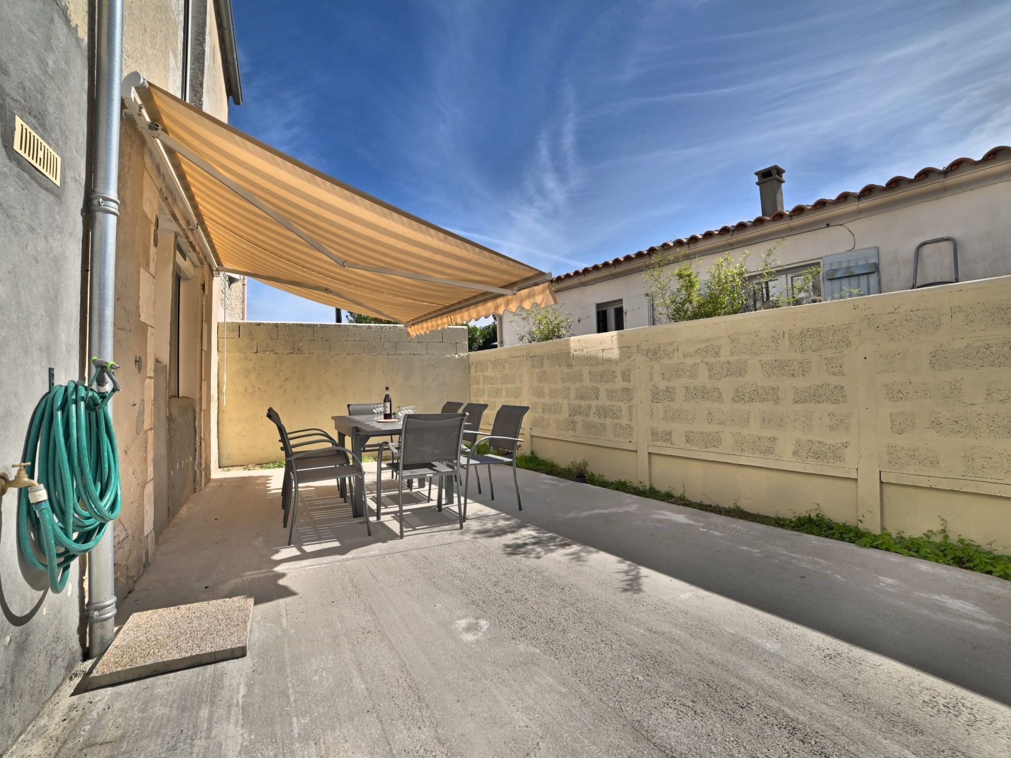 Un patio con una mesa y sillas bajo un toldo a rayas, una manguera y un muro con inscripciones.