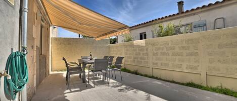 Un patio con una mesa y sillas bajo un toldo a rayas, una manguera y un muro con inscripciones.