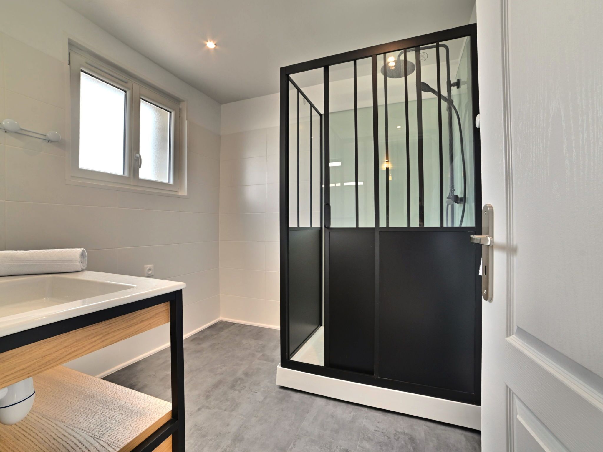 A modern bathroom with a glass shower enclosure, a white sink, and a wooden vanity.