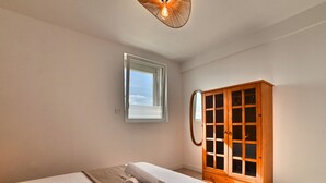A bedroom with a bed, a wooden wardrobe, a window, and a ceiling light fixture.