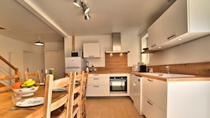 A modern kitchen with white cabinets, a wooden dining table, and a built-in oven.