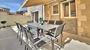 An outdoor patio with a table and chairs, a grill, and a covered area with a striped awning.