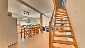 A modern kitchen with wooden flooring, a dining area with a wooden table and chairs, and a wooden staircase.