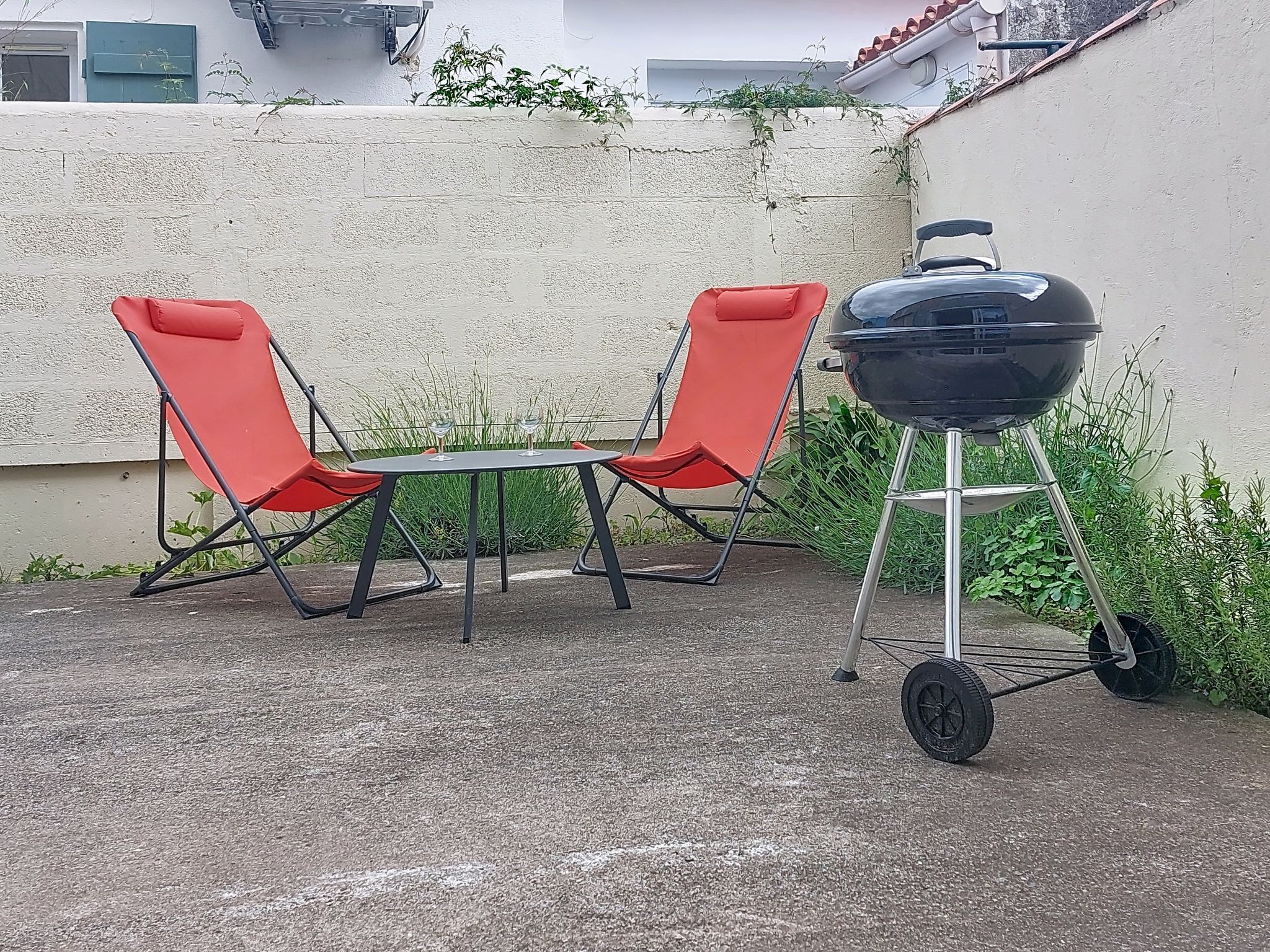 Un patio con dos sillas rojas, una mesita y una parrilla portátil.