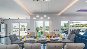 A modern dining area with a large table set for breakfast, featuring fruits, pastries, and beverages. - Villa Mersi (Istria - Pula) (Pula)