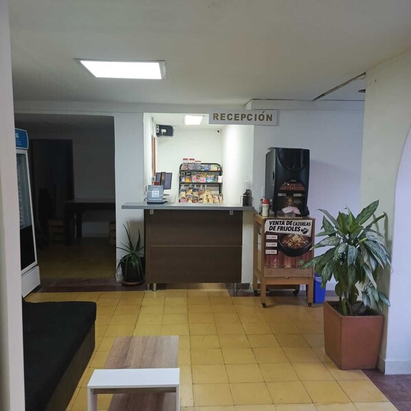A reception area with a counter, a sign reading "RECEPCIÓN", a coffee machine, a plant, and a sign advertising "VENTA DE CAZUELAS DE FRUJOLES". - HOSPEDAJE GIRARDOTA (Girardota)