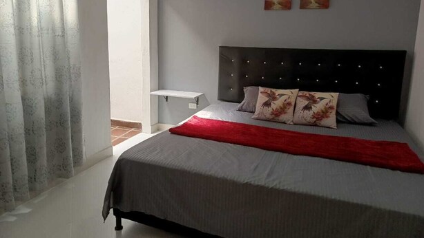 Un dormitorio con cama, mesita de noche y ventana con cortinas.