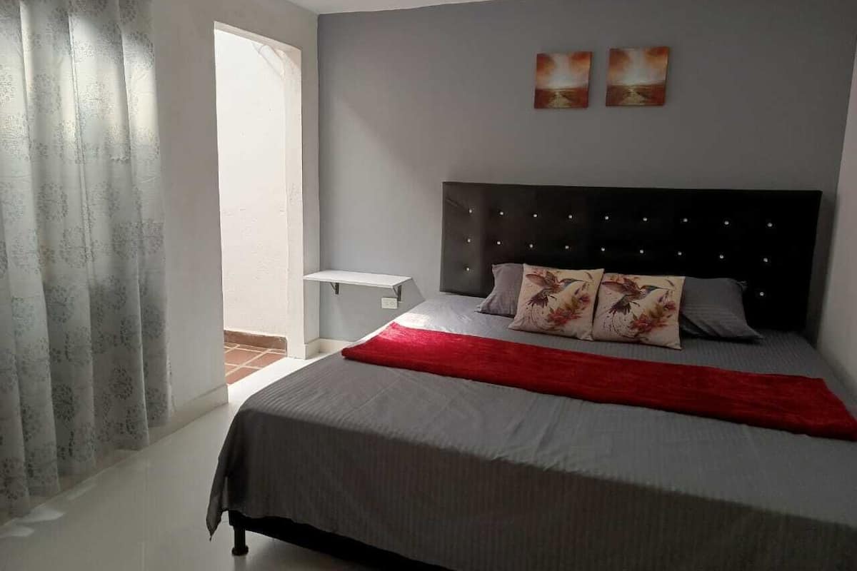 A bedroom with a bed, a nightstand, and a window with curtains.