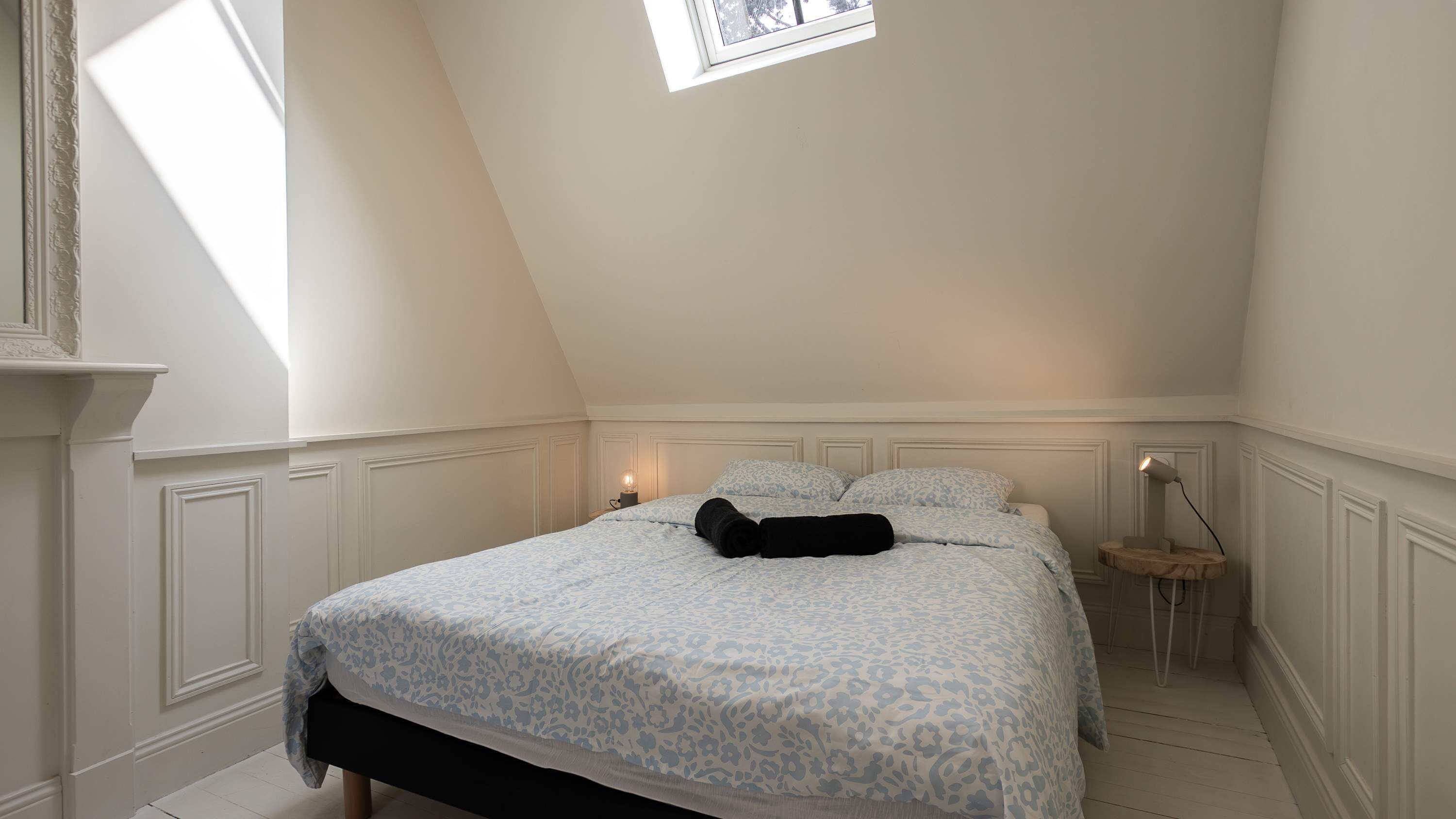 A bedroom with a bed, a nightstand, a lamp, and a window.