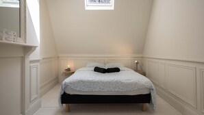 A bedroom with a bed, bedside lamps, a small table, and a window.