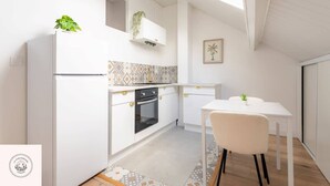 A modern kitchen with white cabinets, a built-in oven, and a dining area with a white table and chair. - Les combles d'Eugene, proche Bollaert, 2pers (Lens)
