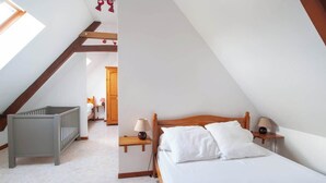 Een slaapkamer met een schuine hemel, een houten bed, nachtkastjes met lampen en een wieg.