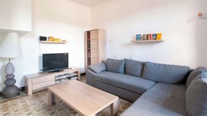 Een moderne woonkamer met een grijze bank, een houten salontafel, een tv op een meubel en een boekenkast vol boeken.