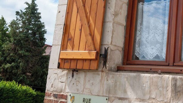 Een gebouw met een houten luik, een bordje met de tekst 'GITE D'ETAPE' en een raam met kantgordijnen.