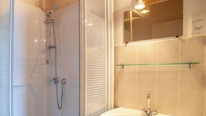 Een badkamer met een douchecabine van glas, een wit wastafelmeubel en een spiegel boven de wastafel.