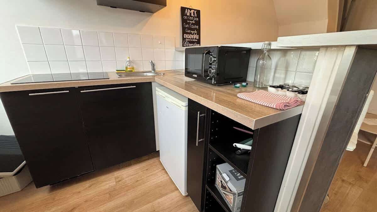 A compact kitchen with a dishwasher, a microwave, and a small oven. There is a sign on the wall and a bottle of dish soap on the counter.