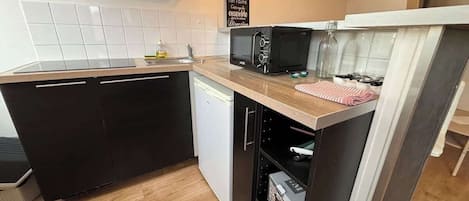 A compact kitchen with a dishwasher, a microwave, and a small oven. There is a sign on the wall and a bottle of dish soap on the counter.