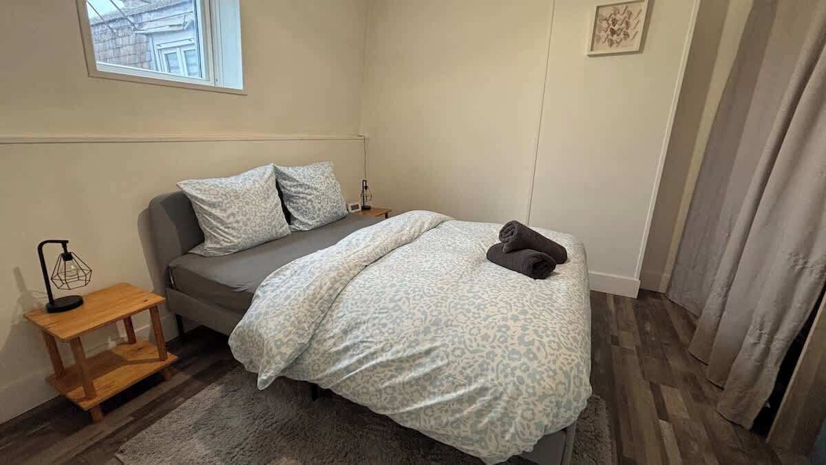 A small, neatly arranged bedroom with a bed, bedside table, and a window.