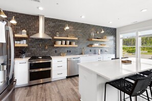 Una cocina moderna con un salpicadero de ladrillo negro, electrodomésticos de acero inoxidable, muebles de cocina blancos y estanterías de madera.