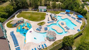 En vy från ovan över ett semesterområde med en stor pool, solstolar, en vattenrutschkana och en paviljong.