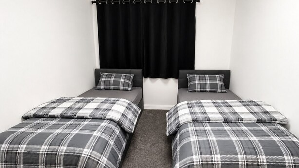 A bedroom with two single beds, each with a black headboard and a grey and white checkered bedspread.