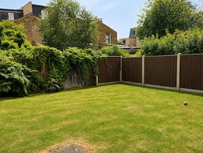 A backyard with a wooden fence, a grassy lawn, and a house in the background.
