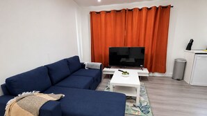A living room with a sofa, a coffee table, a TV, and a trash bin.