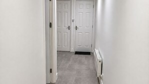 A narrow hallway with two white doors at the end, a radiator on the right wall, and a light fixture on the ceiling.