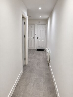 A narrow hallway with two white doors at the end, a radiator on the right wall, and a light fixture on the ceiling.