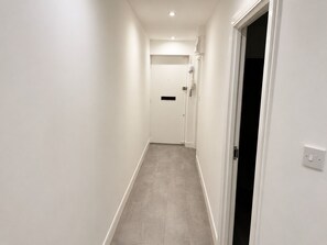 A narrow hallway with a door at the end, a light switch on the wall, and a vent on the ceiling.