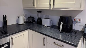 A kitchen with white cabinets, a black countertop, and various appliances including a kettle, toaster, and coffee maker.