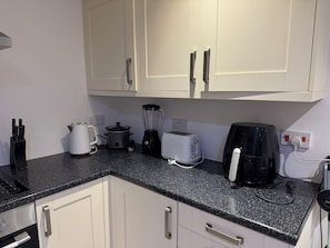 A kitchen with white cabinets, a black countertop, and various appliances including a kettle, toaster, and coffee maker.