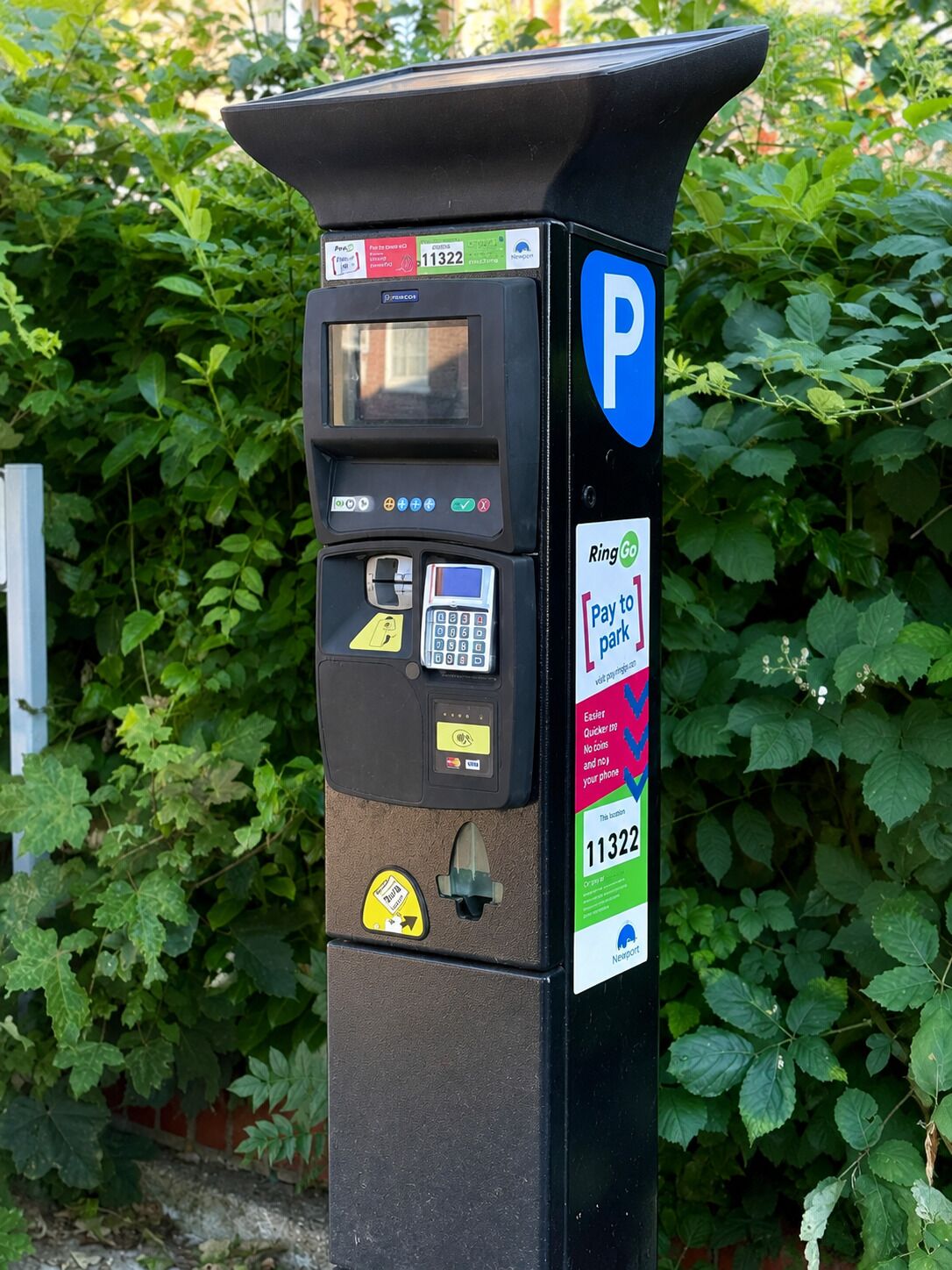 A parking meter with a payment interface, a parking sign, and a sticker indicating a parking zone number.