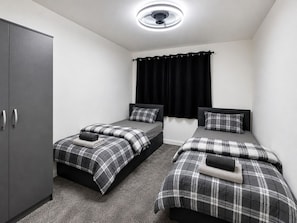 Une chambre avec deux lits simples, une armoire et un luminaire au plafond.