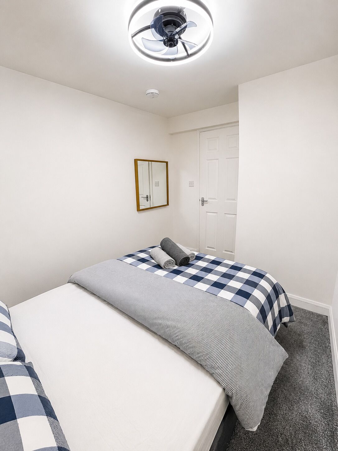 A room with two beds, a ceiling fan, a mirror, and a door.