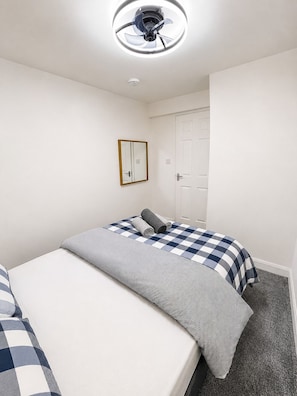 A room with two beds, a ceiling fan, a mirror, and a door.