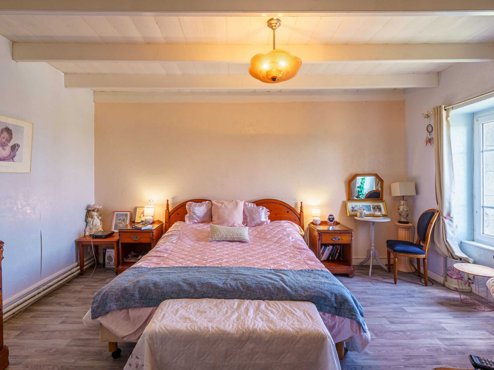 Une chambre à coucher avec un grand lit, des tables de chevet, une chaise, une petite table et une fenêtre avec des rideaux.
