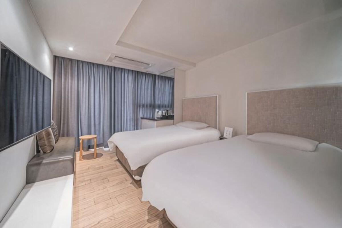 A hotel room with two beds, a small table, a chair, a TV, and a curtain.